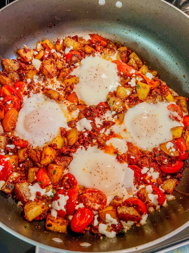 Breakfast skillet cooking on the stove with some fresh eggs on top