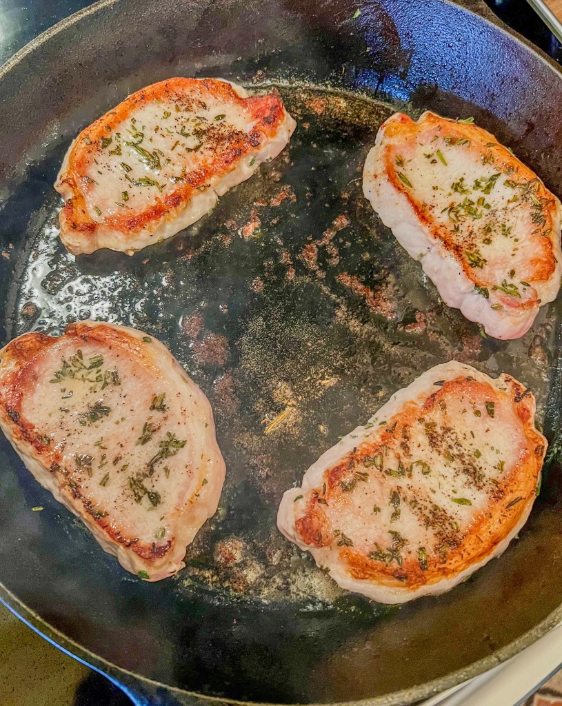 Pork chops cooking in a cast iron skillet on the stove
