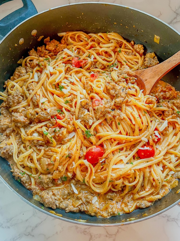 Creamy italian sausage pasta in a skillet with fresh parmesan and parsley scattered on top