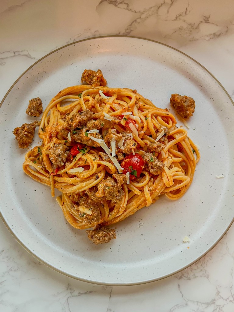 Creamy italian sausage pasta on a white plate with some fresh parmesan and parsley on top
