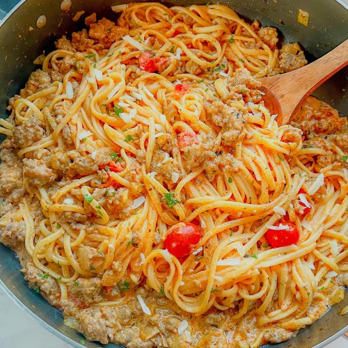 Creamy italian sausage pasta in a skillet with fresh parmesan and parsley scattered on top