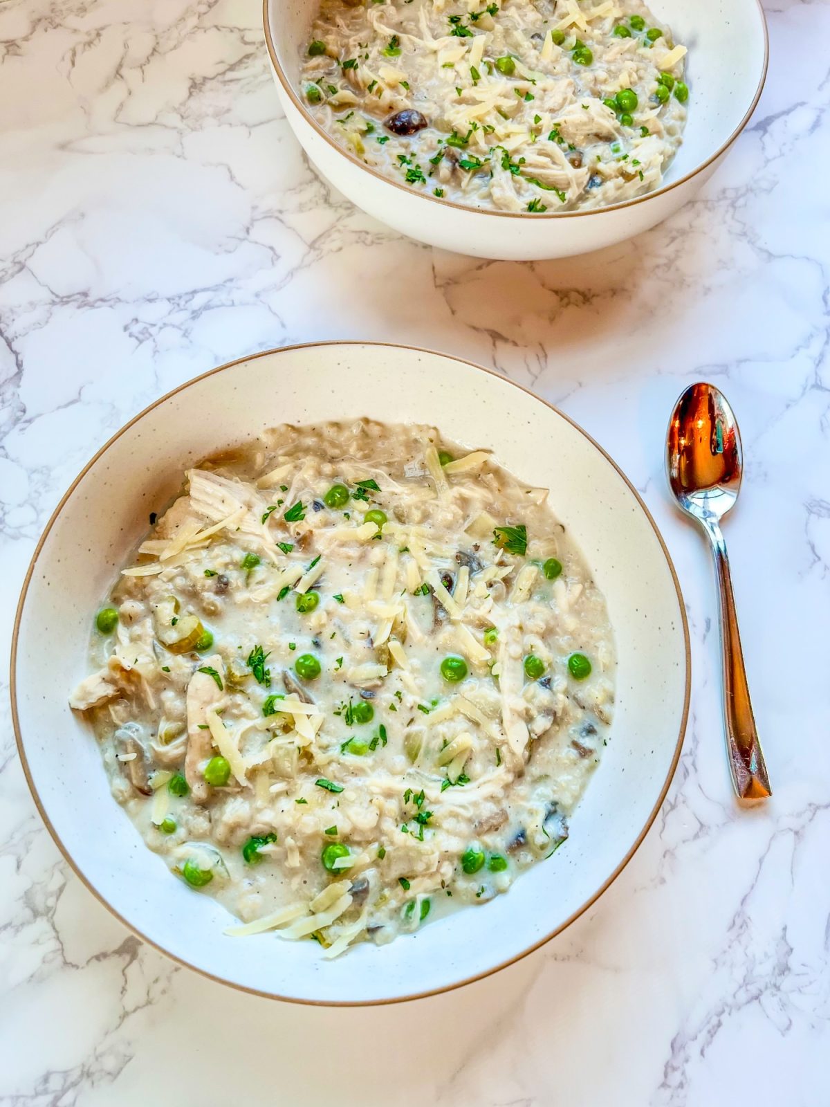 Crockpot creamy chicken and rice soup in a bowl with a spoon next to it and another bowl behind
