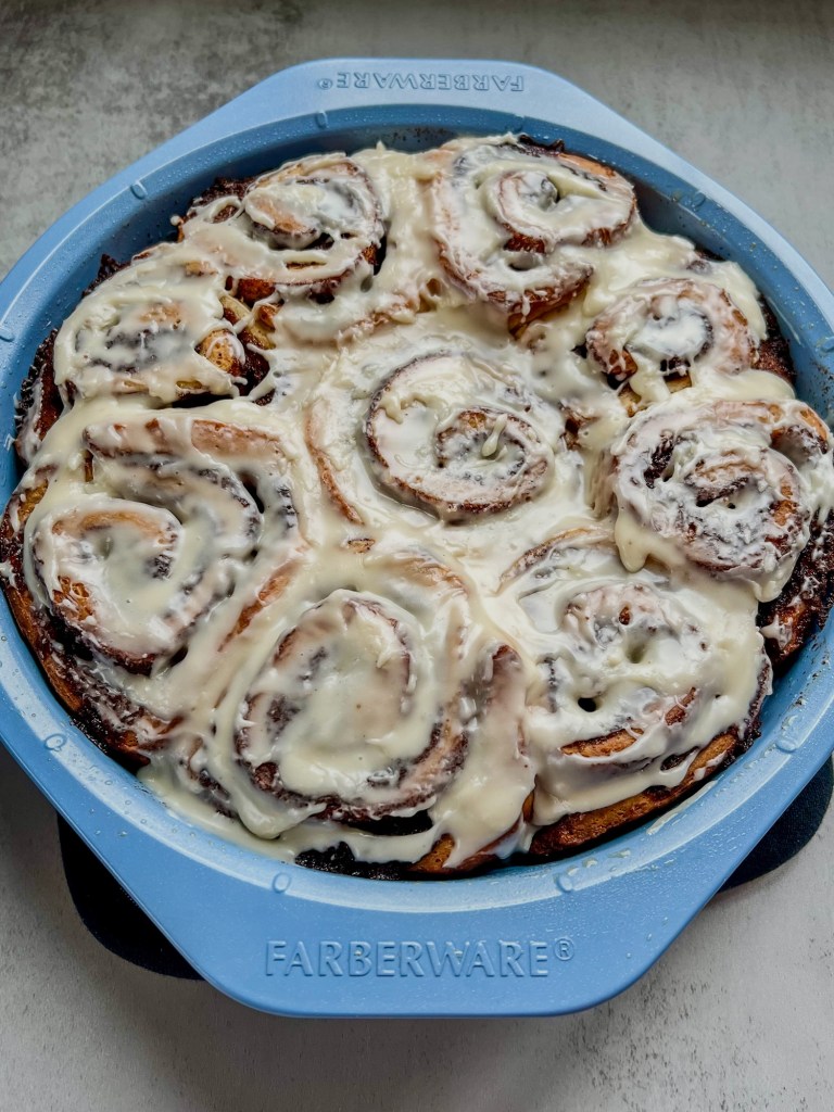 Eggnog Cinnamon Rolls with eggnog icing in a blue cake pan on a countertop