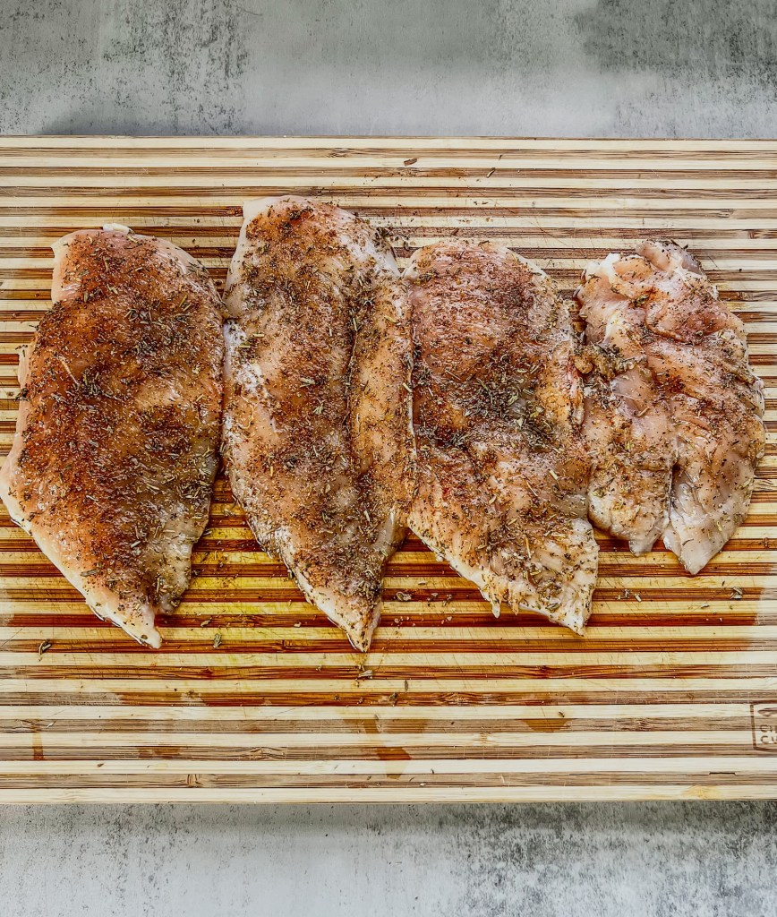 Chicken breasts on a cutting board that have been coated in seasonings
