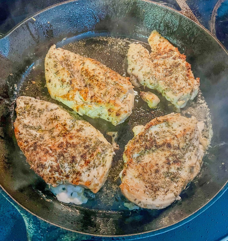 Chicken breast cooking on the stove in a cast iron skillet