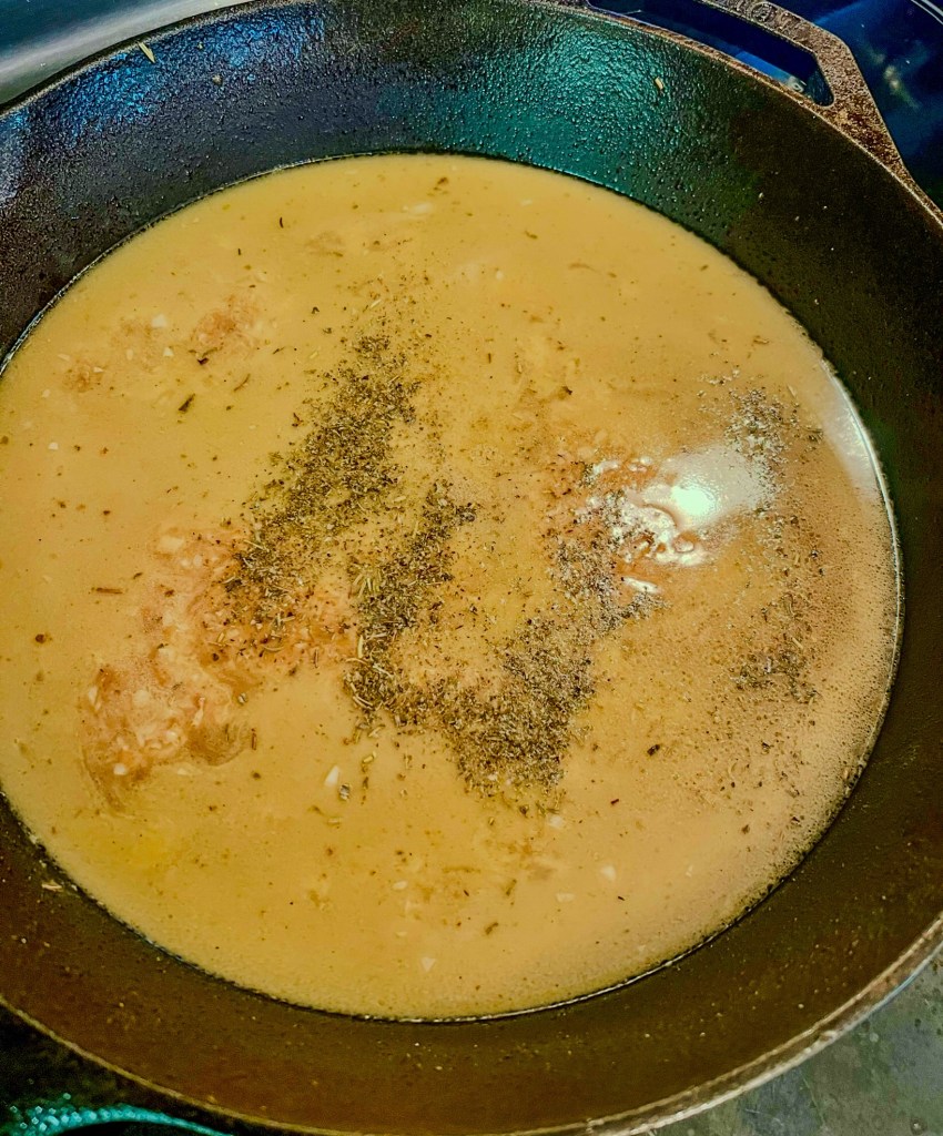 Broth, butter, garlic, seasonings, and cheese cooking in a cast iron skillet