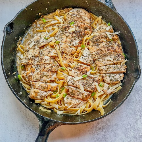 Garlic chicken pasta with green onion and parmesan for garnish in a cast iron skillet sitting on a countertop