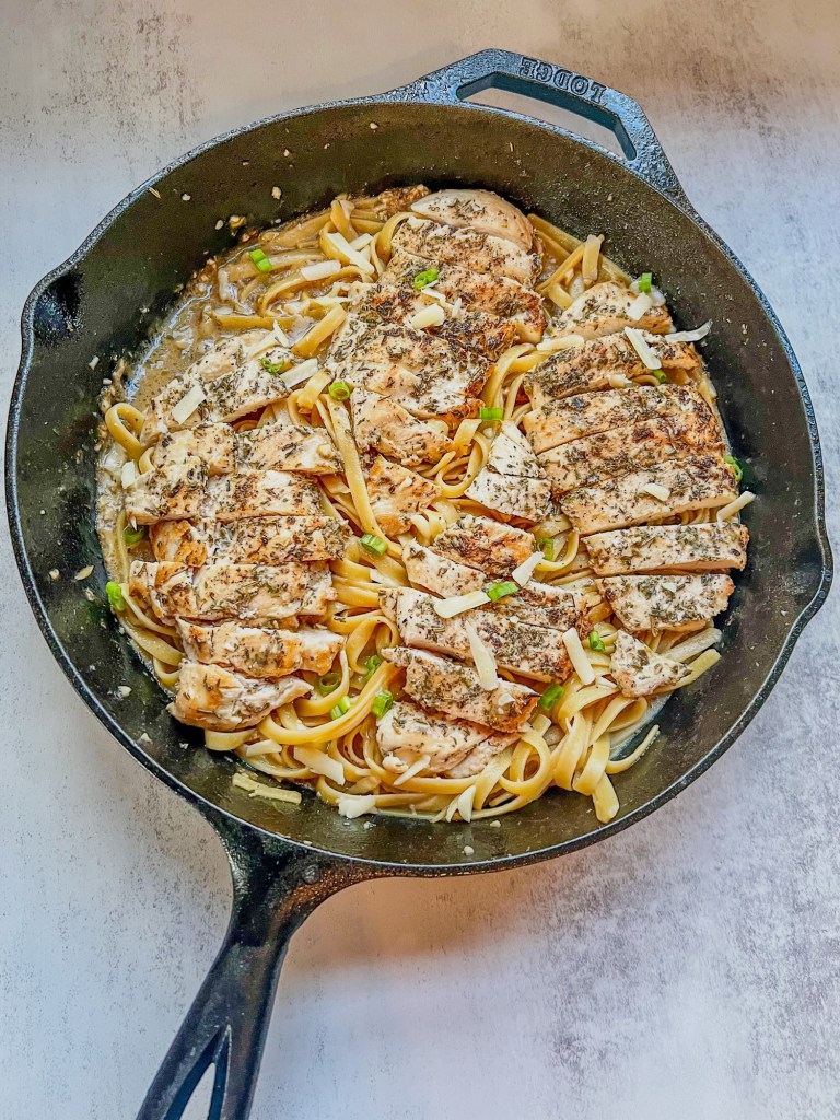 Garlic chicken pasta with green onion and parmesan for garnish in a cast iron skillet sitting on a countertop