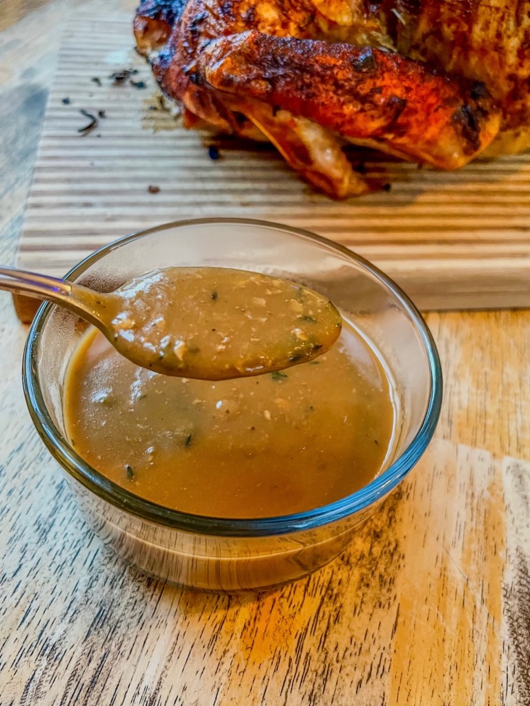 Gravy in a small dish with a spoon scooping some with a roasted turkey behind