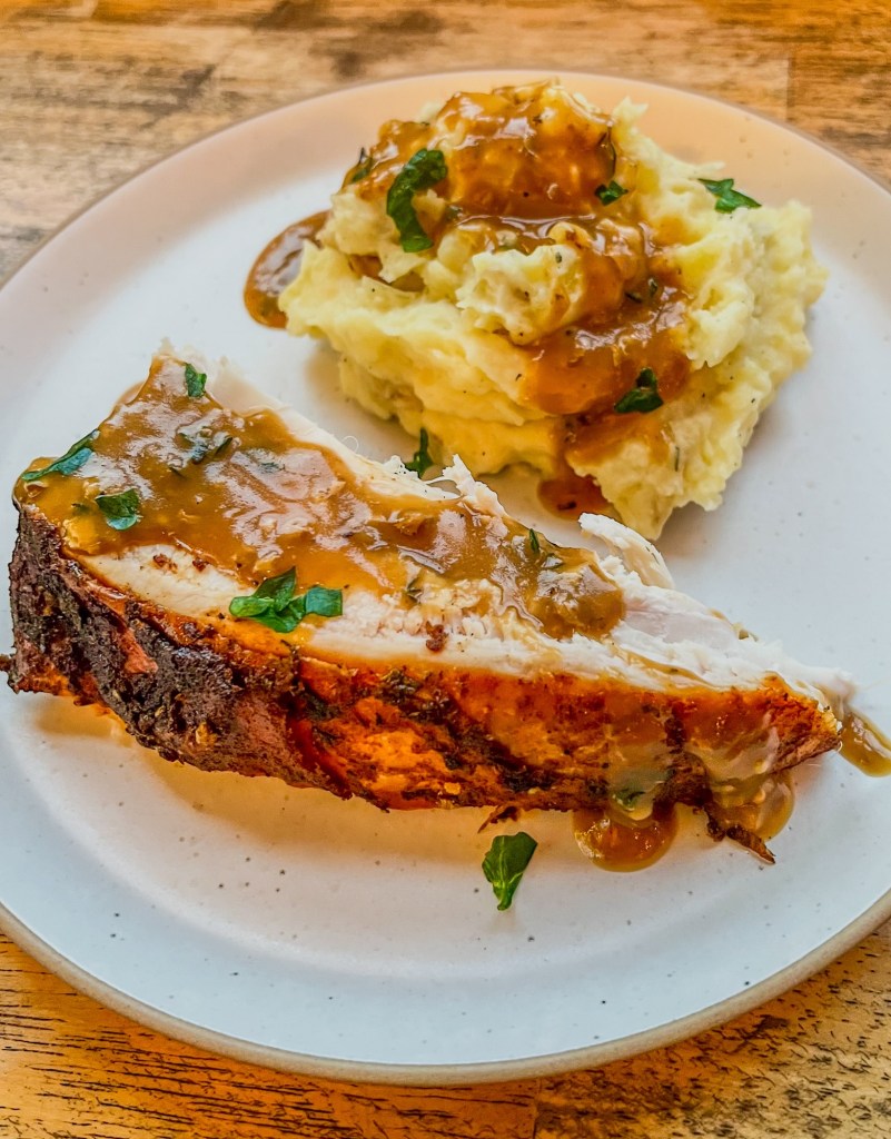 Turkey with mashed potatoes and gravy on a white plate on a wooden table