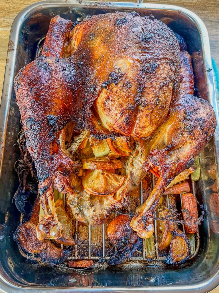 Garlic herb roasted turkey that's just been removed from the oven, in a pan with some roasted veggies and herbs