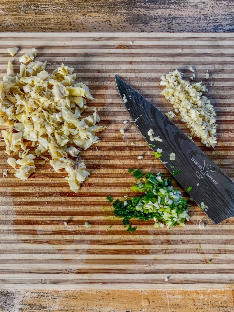 Green onion, garlic, and artichokes cut up on a wooden cutting board
