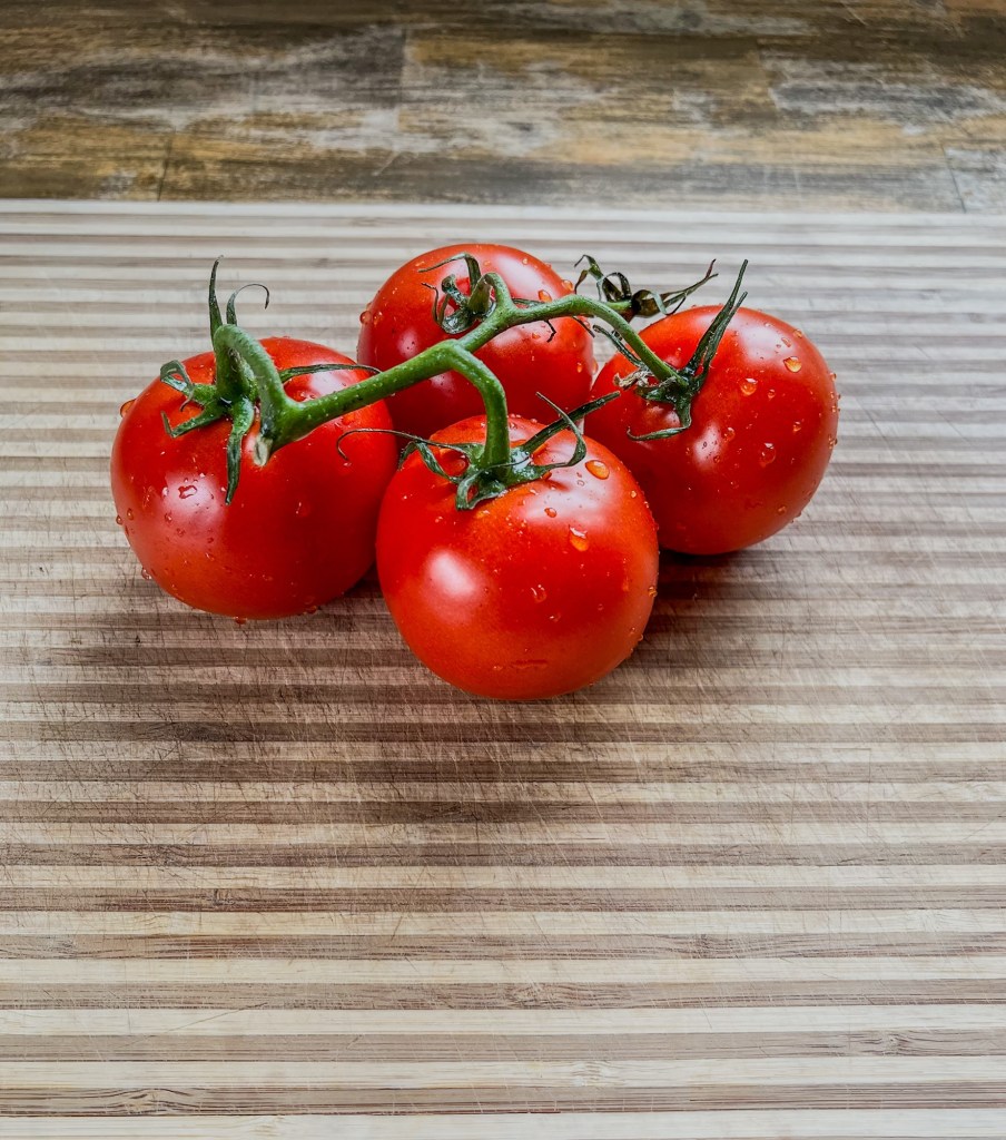 Tomatoes on the vine after just getting washed, on a wooden cutting board