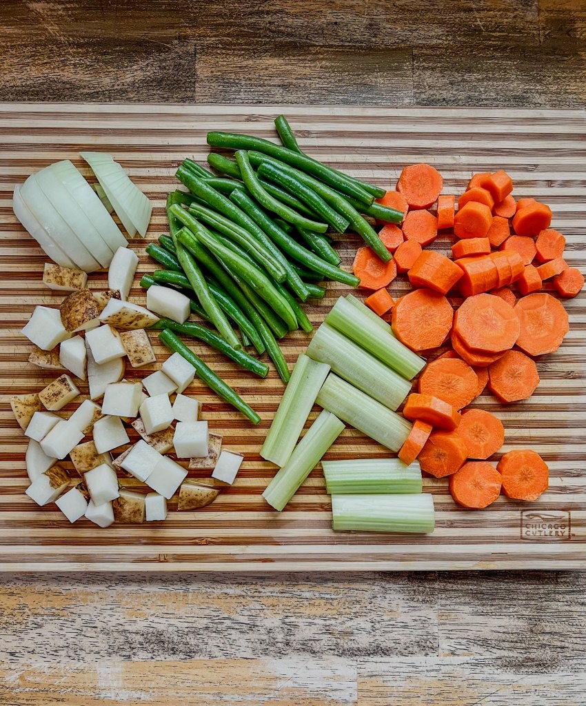 Carrots, beans, onion, potatoes, and celery chopped up on a wooden cutting board