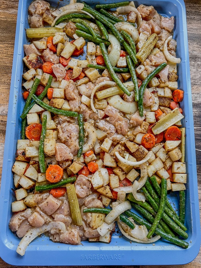 A blue sheet pan filled with chicken and veggies before going into the oven
