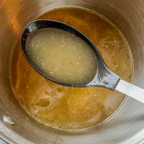 Homemade Turkey Stock in a large pot with a spoon scooping some out