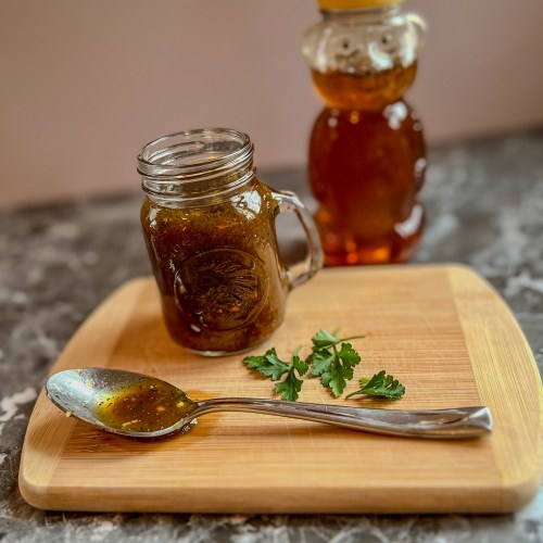Honey balsamic vinaigrette in a small jar with a spoonful of it and some herbs next to it