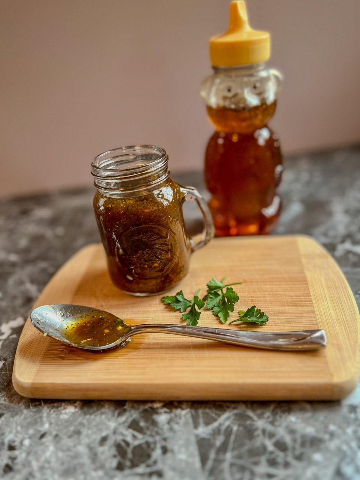 Honey balsamic vinaigrette in a small jar with a spoonful of it and some herbs next to it