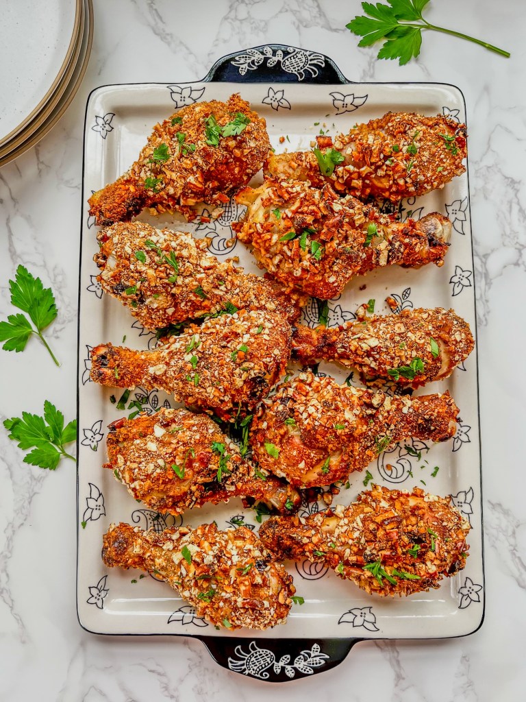 Honey mustard chicken drumsticks on a platter with some fresh parsley and white plates stacked up behind