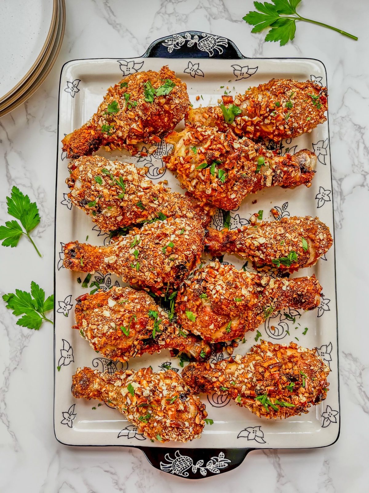 Honey mustard chicken drumsticks on a platter with some fresh parsley and white plates stacked up behind