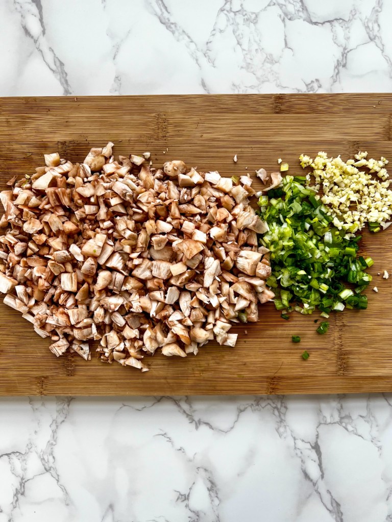 Mushrooms, green onion, and garlic cut up on a cutting board