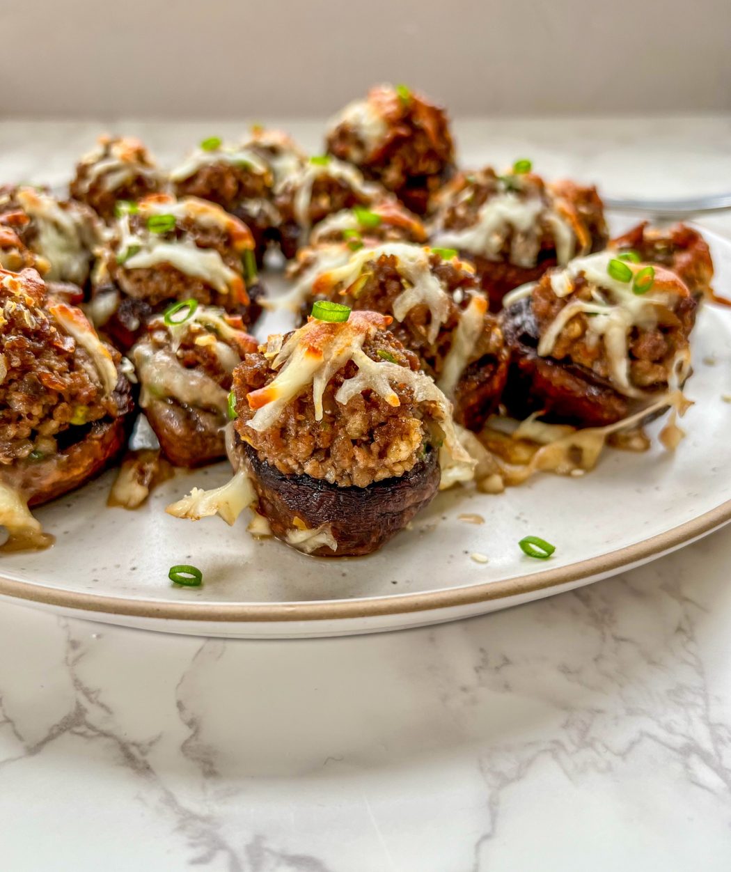 Korean stuffed mushrooms on a plate with some sesame seeds and thinly sliced green onion for garnish