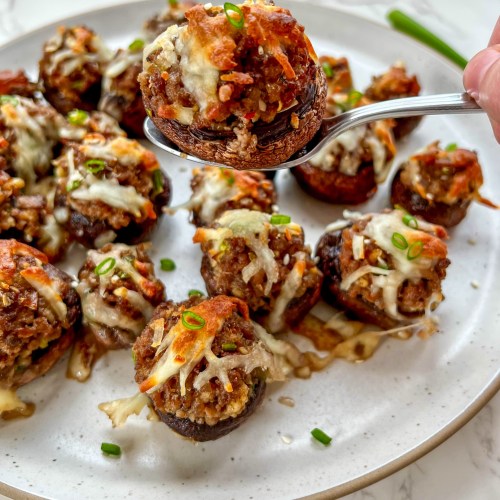Korean stuffed mushrooms on a plate with some sesame seeds and green onion for garnish with a spoon scooping a mushroom up to eat