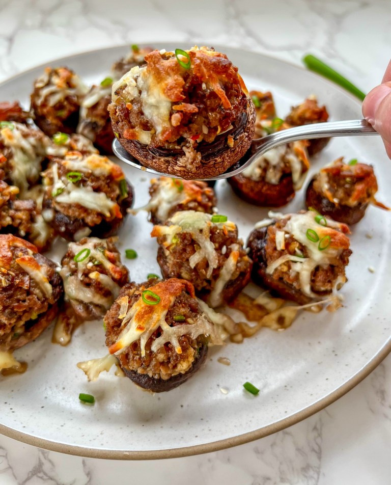 Korean stuffed mushrooms on a plate with some sesame seeds and green onion for garnish with a spoon scooping a mushroom up to eat