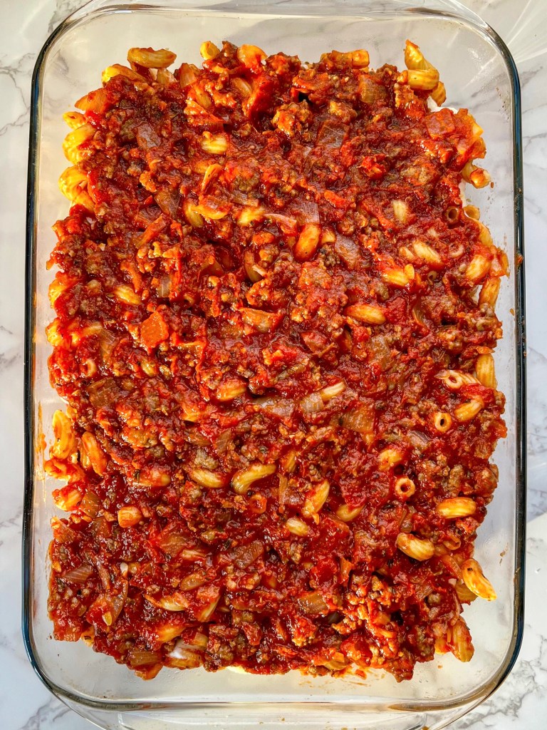 Baked ziti being layered in a pan