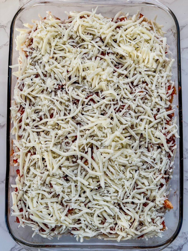 Lasagna bake with shredded mozzarella scattered on top, just before going into the oven