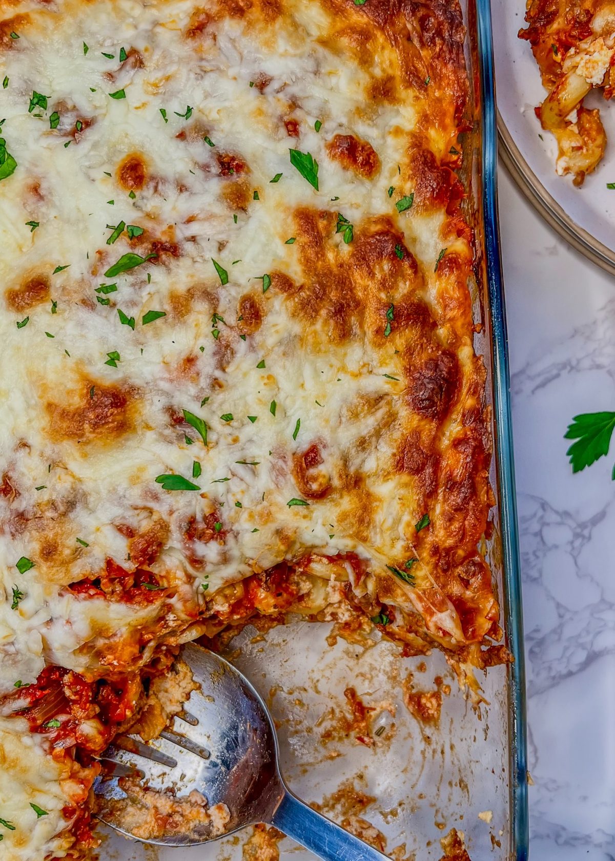 Lasagna Style Baked Ziti in a pan with some scooped out onto a plate nearby
