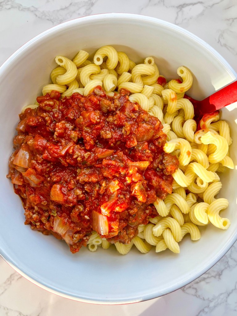 Cavatappi pasta in a bowl with a tomato meat sauce before being combined