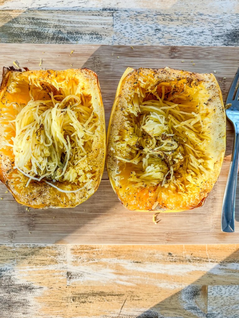 Spaghetti squash being shredded with a fork on a cutting board