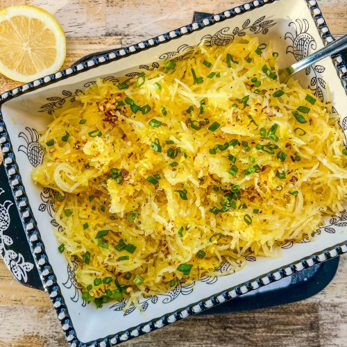 Lemon garlic air fryer spaghetti squash in a dish topped with chives, black pepper, crushed red pepper, lemon zest and juice