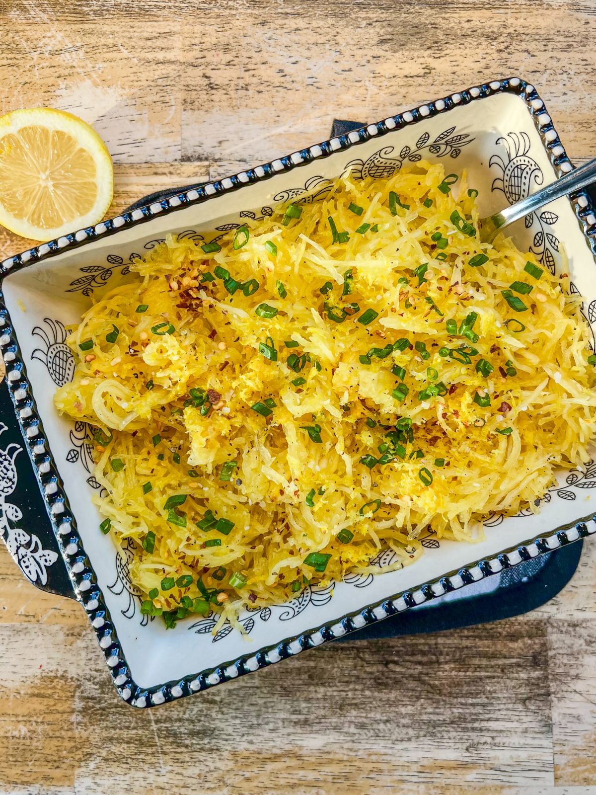 Lemon garlic air fryer spaghetti squash in a dish topped with chives, black pepper, crushed red pepper, lemon zest and juice