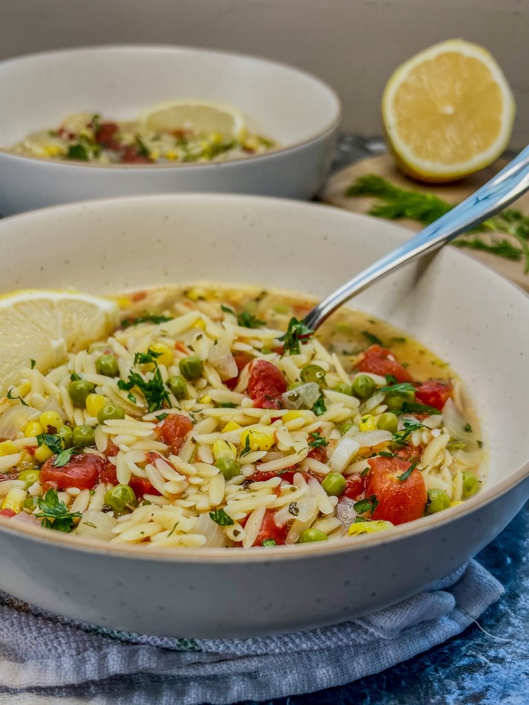 Lemon orzo soup dished into bowls with some fresh lemon and dill nearby on a cutting board
