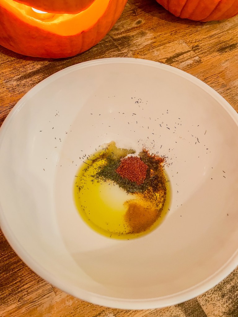 Seasonings and oil in a large mixing bowl on a wooden table with some pumpkins behind it