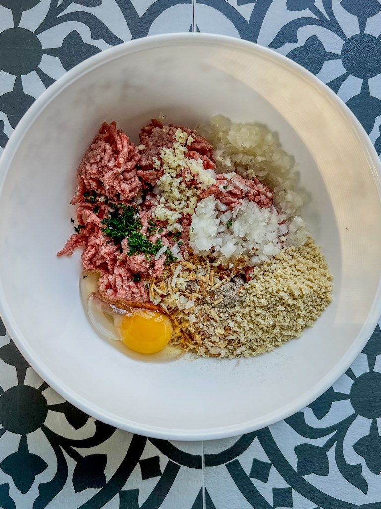 A mixing bowl filled with burger patty ingredients before being mixed