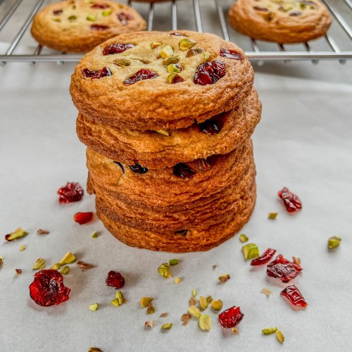 Orange cranberry pistachio cookies stacked up with some pistachios and cranberries scattered around