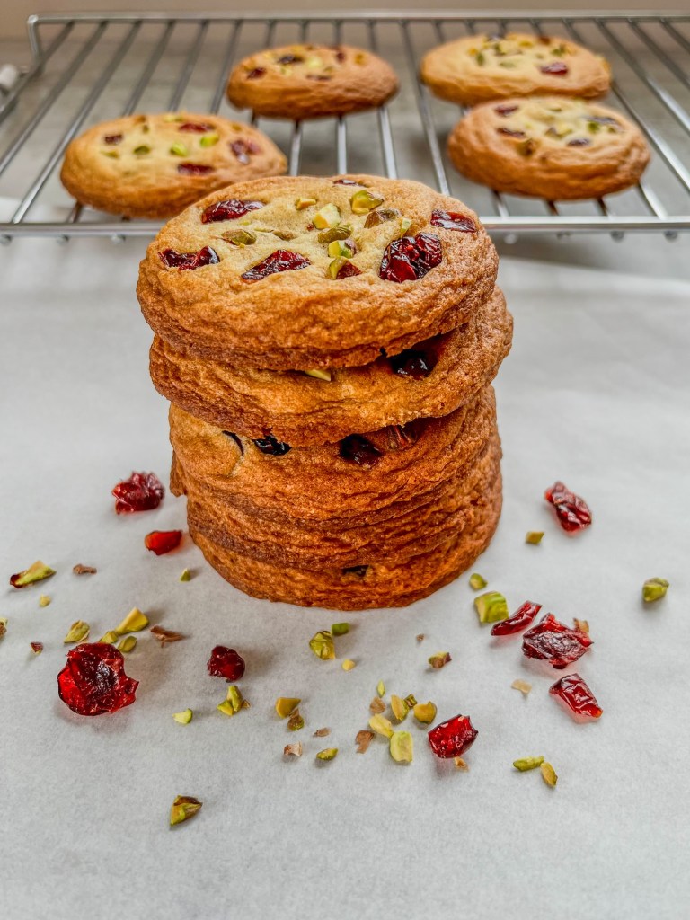 Orange cranberry pistachio cookies stacked up with some pistachios and cranberries scattered around
