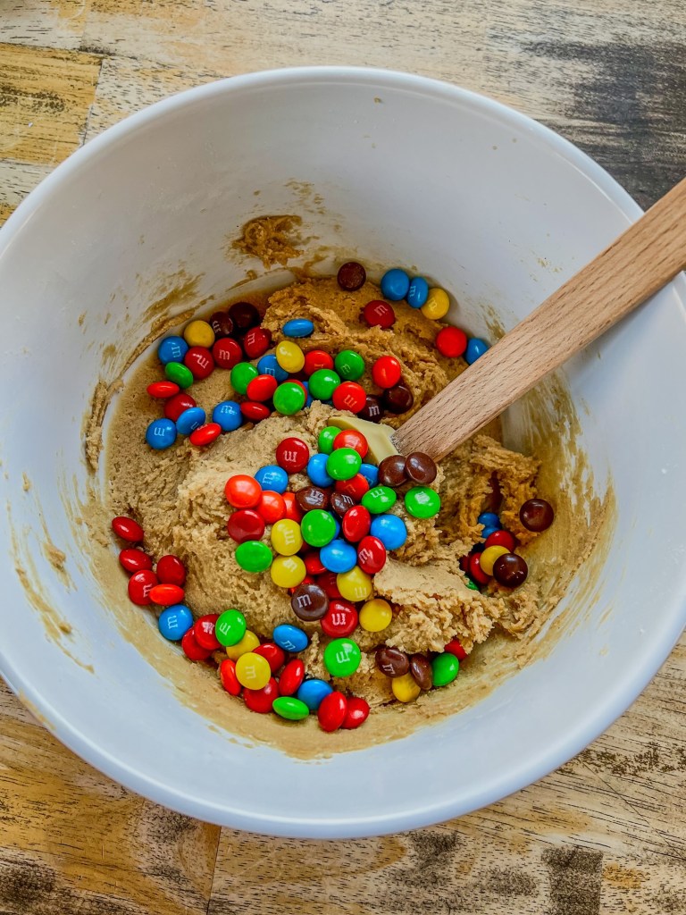 Peanut butter m&m cookie batter in a bowl with a rubber spatula inside
