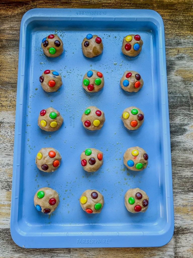 A blue baking sheet with peanut butter m&m cookie dough balls on it