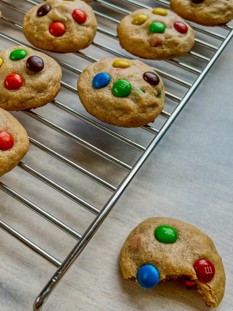 Peanut butter m&m cookies on a rack on top of some parchment paper, on a wooden table