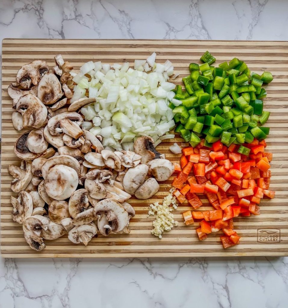 Mushrooms, peppers, onion, and garlic chopped up on a wooden cutting board