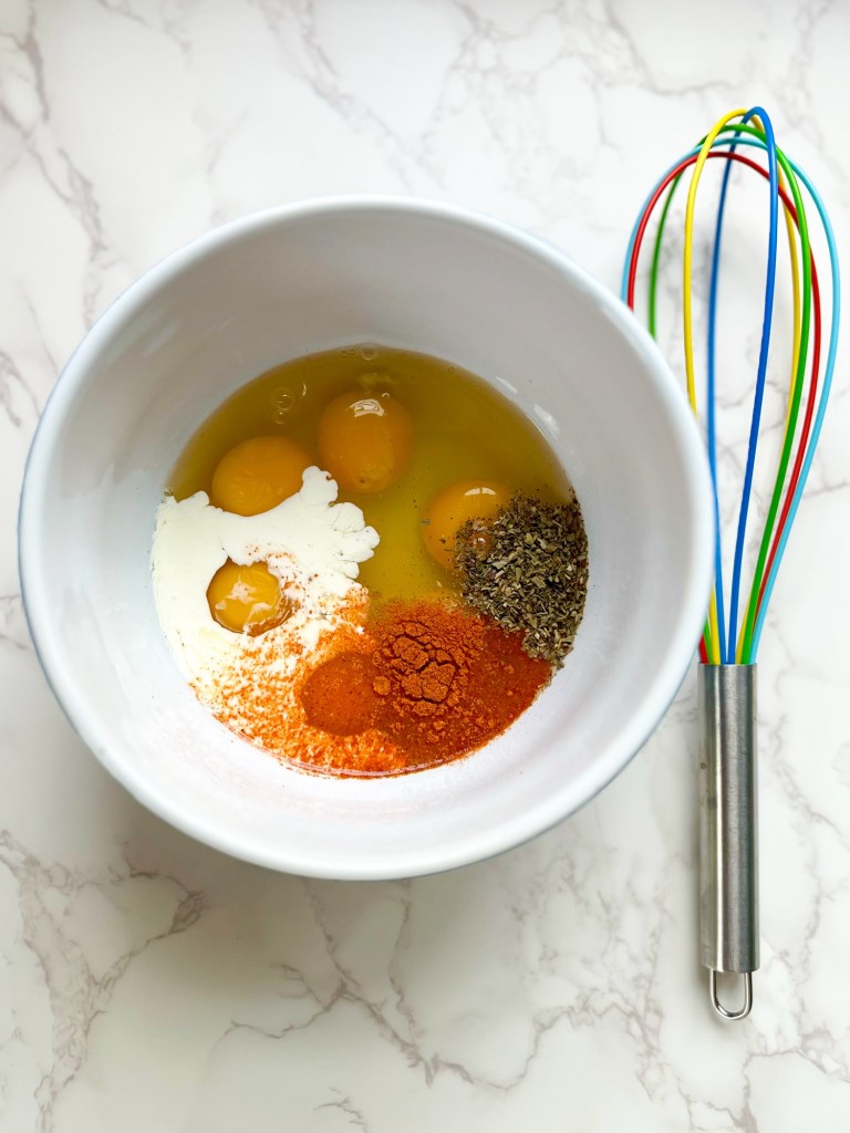 Eggs, cream, cheese, and seasonings in a mixing bowl with a whisk nearby