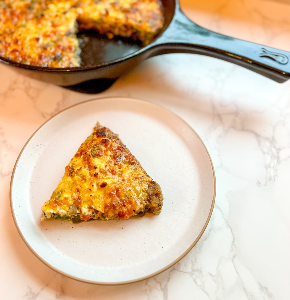 Sausage and veggie frittata cut into a slice on a plate with a pan filled with more behind