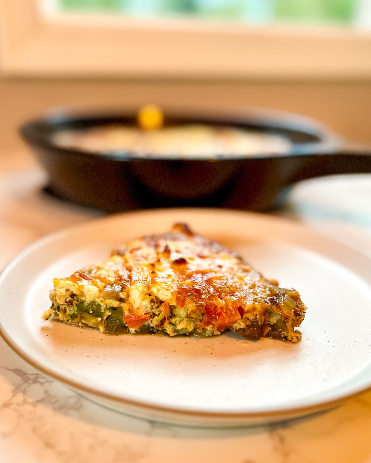 Sausage and veggie frittata cut into a slice on a plate with a pan filled with more behind it