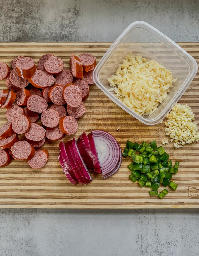 Sausage, veggies, and shredded cheese on a wooden cutting board
