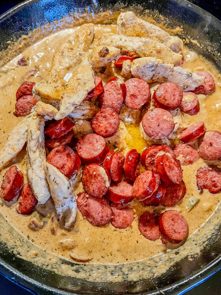 Chicken and sausage freshly added into a skillet just before pasta is added