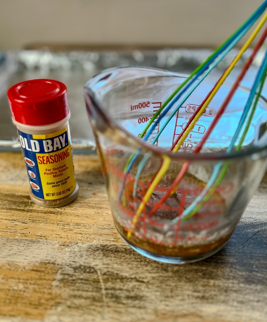A measuring cup filled with melted butter and seasonings with some old bay next to it on the table